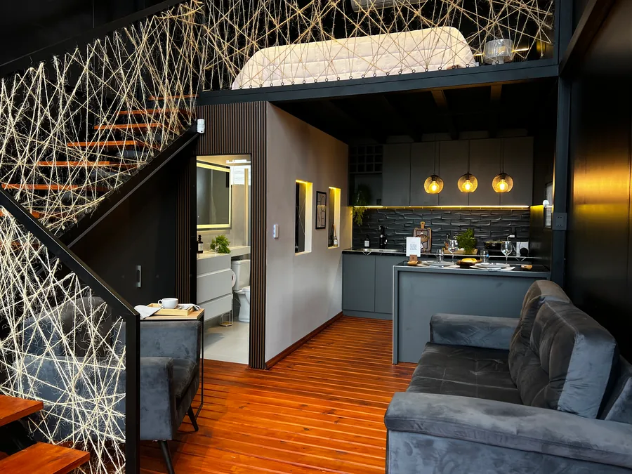 Interior de The Loft: estar, cocina y escalera al entrepiso con baranda de hilos